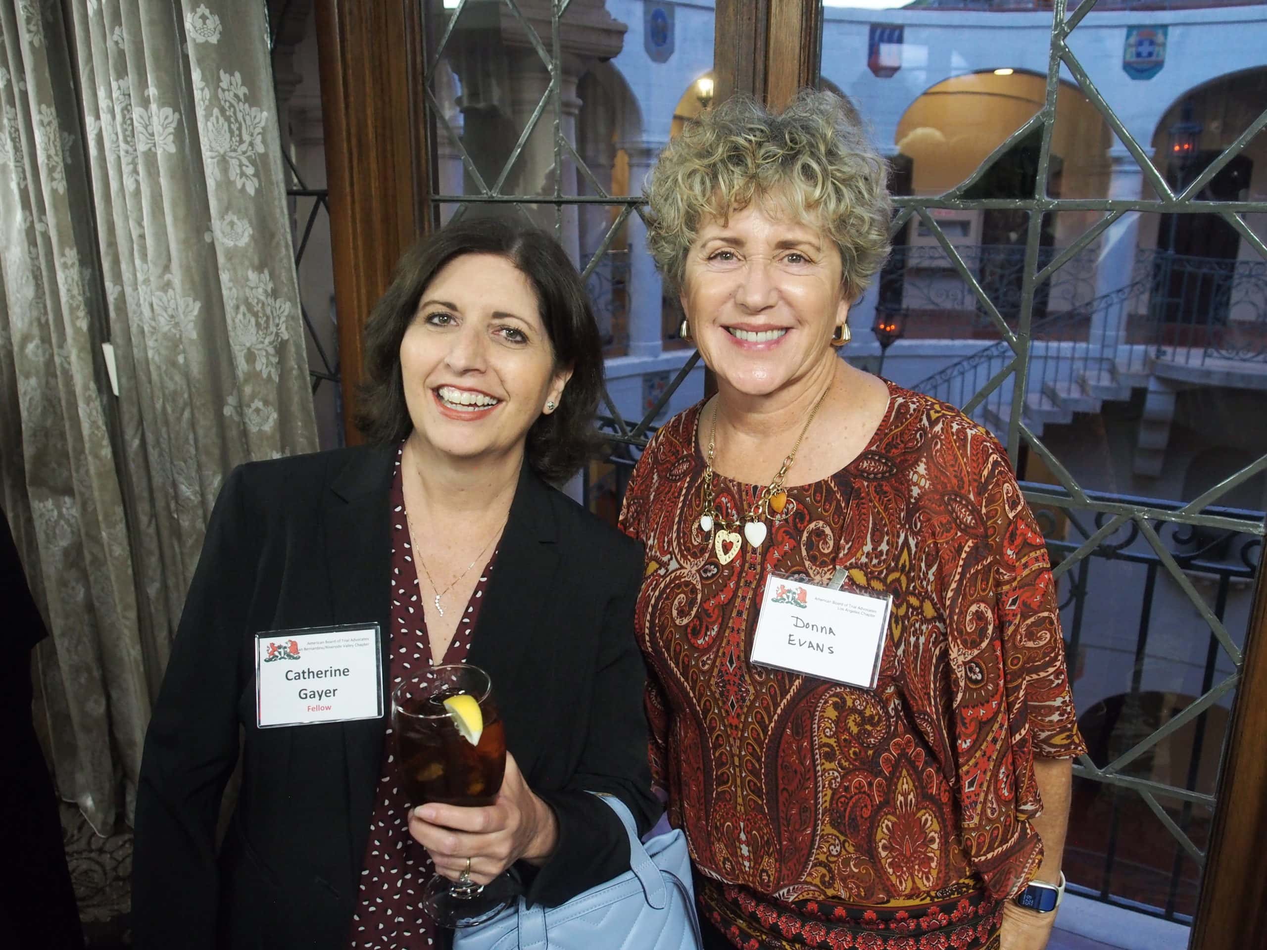 Two women smile in front of a window.