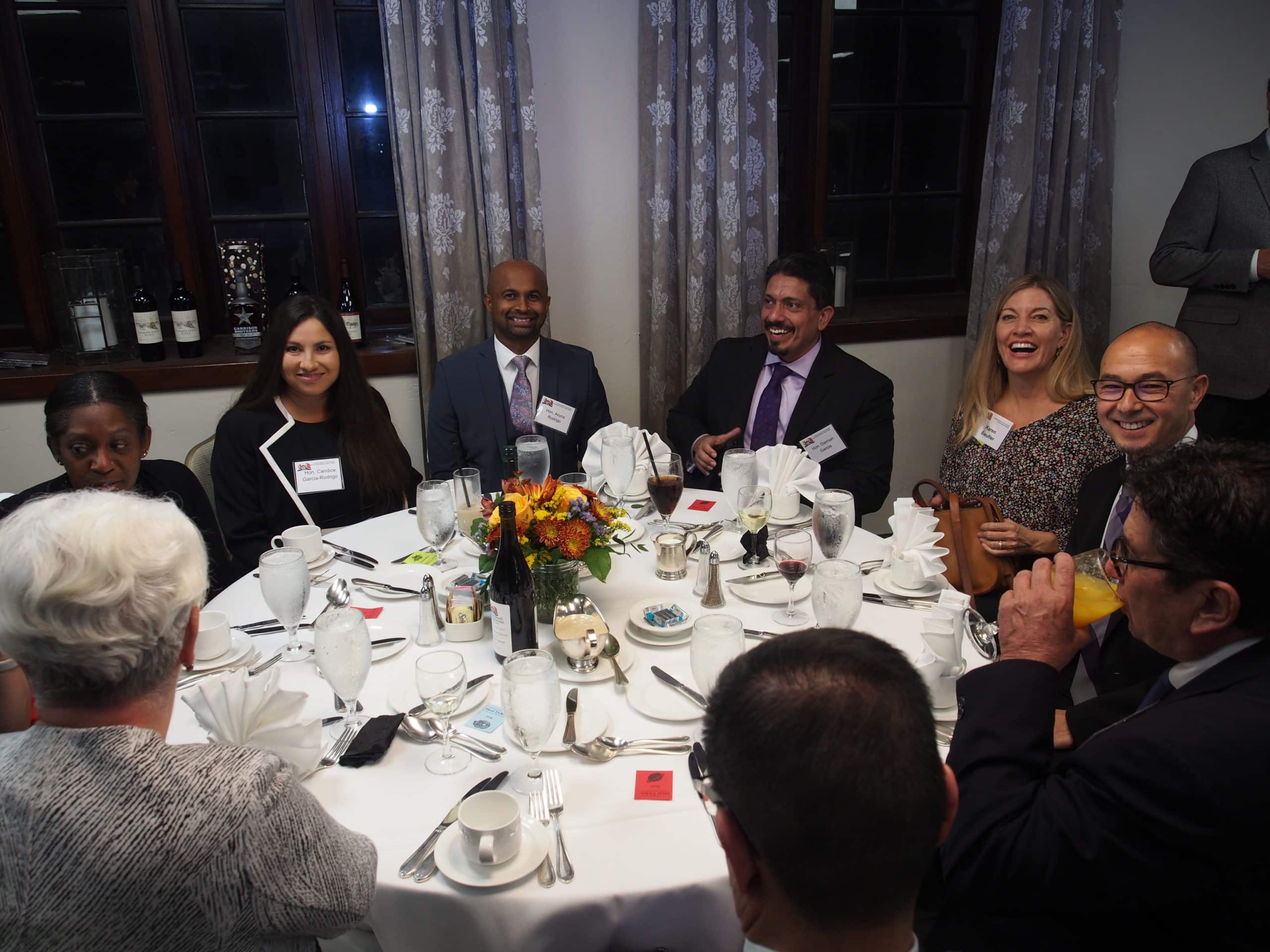 Nine people sit around a table with a white tablecloth and water glasses.